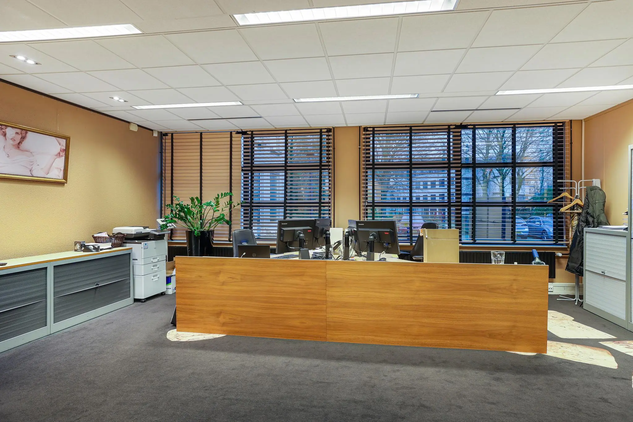 Modern kantoor aan de Oude Utrechtseweg met een houten balie, meerdere bureaus en grote ramen met jaloezieën.